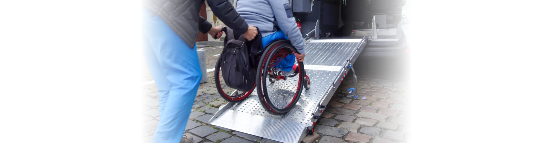 Assistant helping disabled person on wheelchair with transport using accessible van ramp