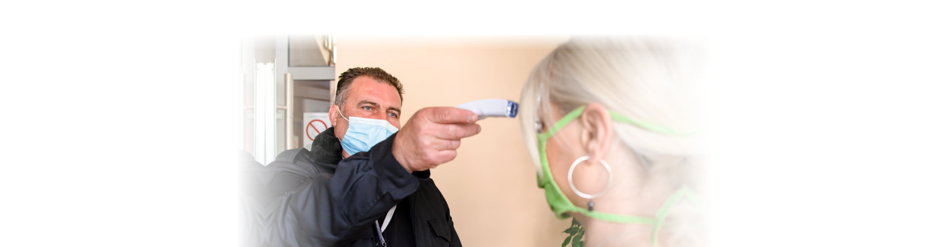 Male security measuring body temperature of female worker on the entrance.